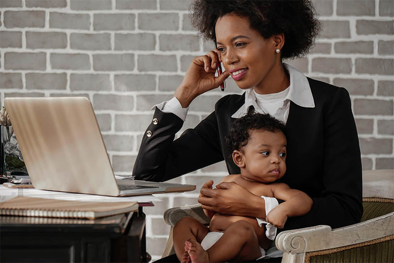 mother holding her baby while working on a laptop